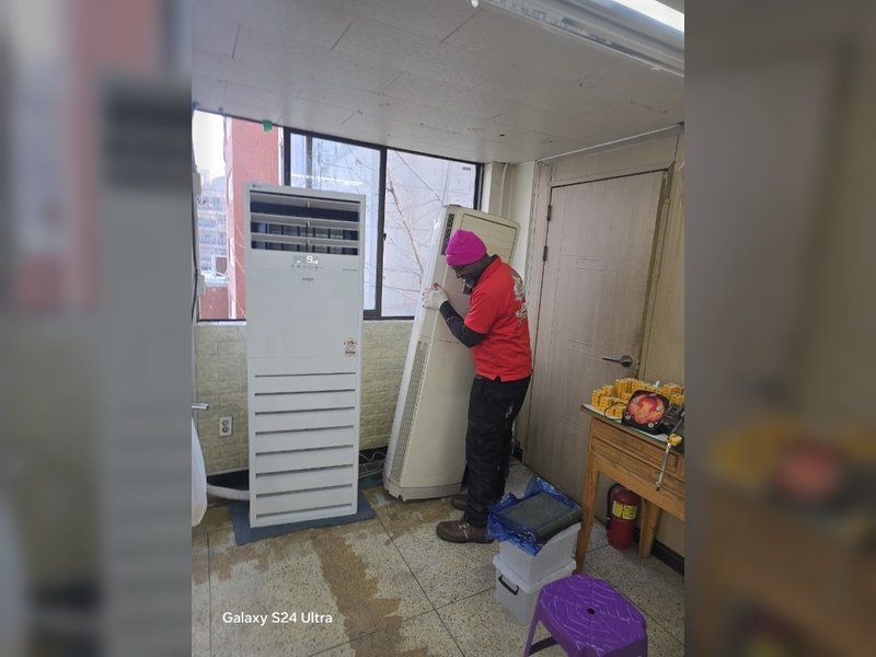 한 작업자가 실내에서 오래된 스탠드형 에어컨을 해체하거나 이동시키는 작업을 진행 중이다.<br>