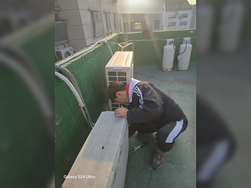 한 작업자가 옥상에서 스패너를 이용해 실외기를 해체하거나 수리하는 작업을 하고 있다.<br>