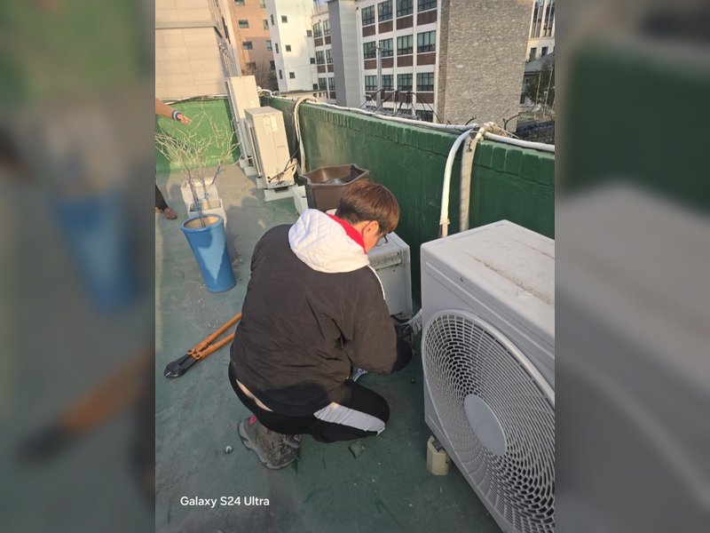 한 작업자가 옥상에서 대형 볼트 커터를 사용하여 실외기를 해체하는 작업을 진행 중이다.<br>
