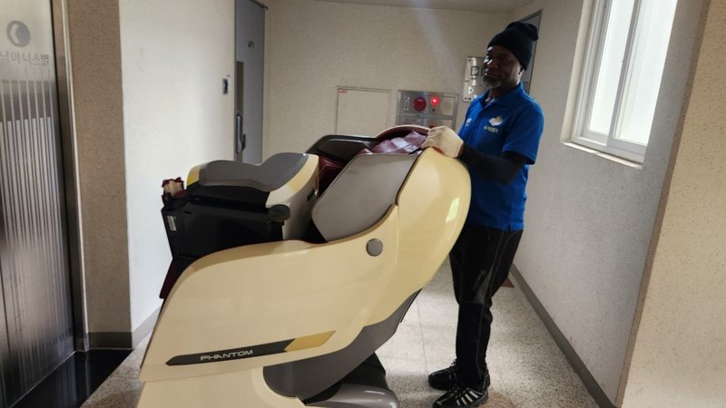 작업자가 복도에서 안마의자를 운반하고 있는 중